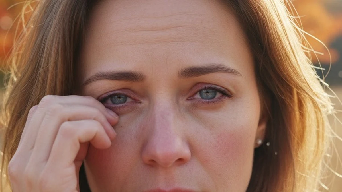 Close-up of a woman's red, watery eyes as she rubs one eye, showing signs of ocular allergy or dry eye irritation